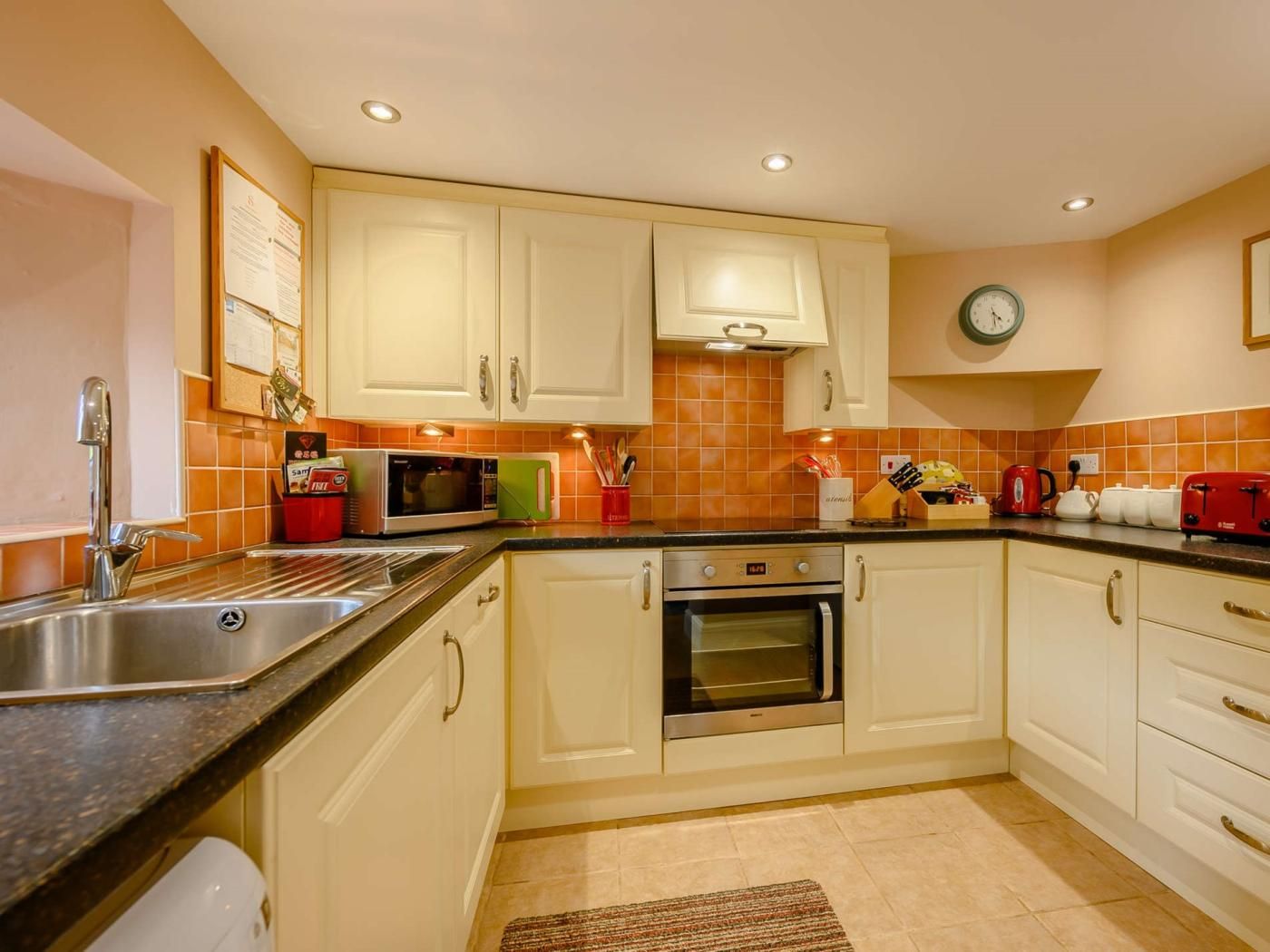 A kitchen with white cabinets, a stainless steel sink, a microwave, an oven, and a red toaster.