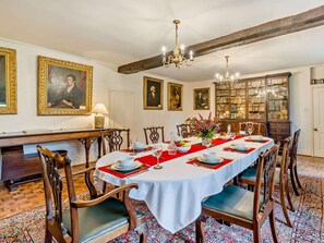 A dining room with a long table set for a meal, surrounded by chairs, with a chandelier above and a bookshelf in the background. - 4 Bed in Holmrook (oc-sz158) (Eskdale)
