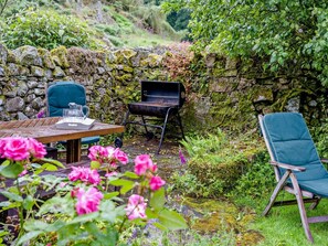 A rustic outdoor seating area with a stone wall, a grill, and a table with chairs. - 4 Bed in Holmrook (oc-sz158) (Eskdale)