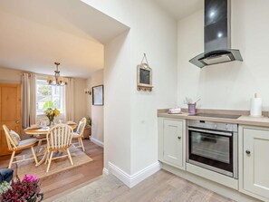 A modern kitchen with a built-in oven, a dining area with a wooden table and chairs, and a window with curtains. - 2 Bed in Cockermouth (oc-93280) (Bridekirk)