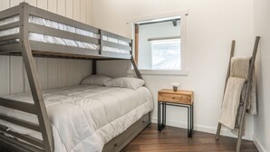 A bunk bed with a wooden frame and white bedding, a small wooden nightstand with a vase, a ladder against the wall, and a window with a view. - Remodeled 1BD+Loft, Sleeps 5, Walk to Town Center + Pool, Spa, Sauna, & Laundry (Mammoth Lakes)
