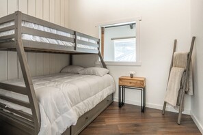 Ein Stockbett mit Holzrahmen und weißer Bettwäsche, ein kleiner Nachttisch mit einer Vase, eine an der Wand stehende Leiter und ein Fenster mit Blick.