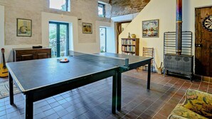 Une pièce avec une table de ping-pong, un jeu de fléchettes, une bibliothèque, une guitare et un mur en pierre rustique.