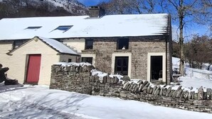 Un bâtiment en pierre avec une porte rouge, un mur en pierre et un toit recouvert de neige.
