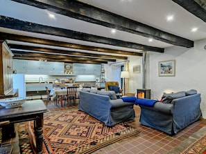 Ein Wohnzimmer mit einer Sofagarnitur, einem gemusterten Teppich und einer Küche im Hintergrund.
