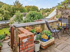 A rooftop patio with a brick wall, potted plants, a table with chairs, and a view of the surrounding greenery.