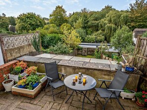 A patio with a round table and two chairs, surrounded by potted plants and a brick wall.