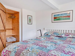 A bedroom with a wooden wardrobe, a bed with a colorful quilt, a framed painting, and a white radiator.