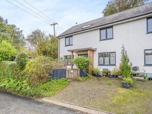 Een woonhuis met twee verdiepingen, een voortuin met terras, een grindpad en verschillende potplanten.