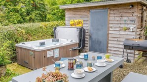 Een bubbelbad, een barbecue en een tafel gedekt met eten en drinken in een tuin.