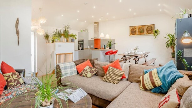Een moderne woonkamer met een hoekbank, een eethoek en een keuken op de achtergrond.