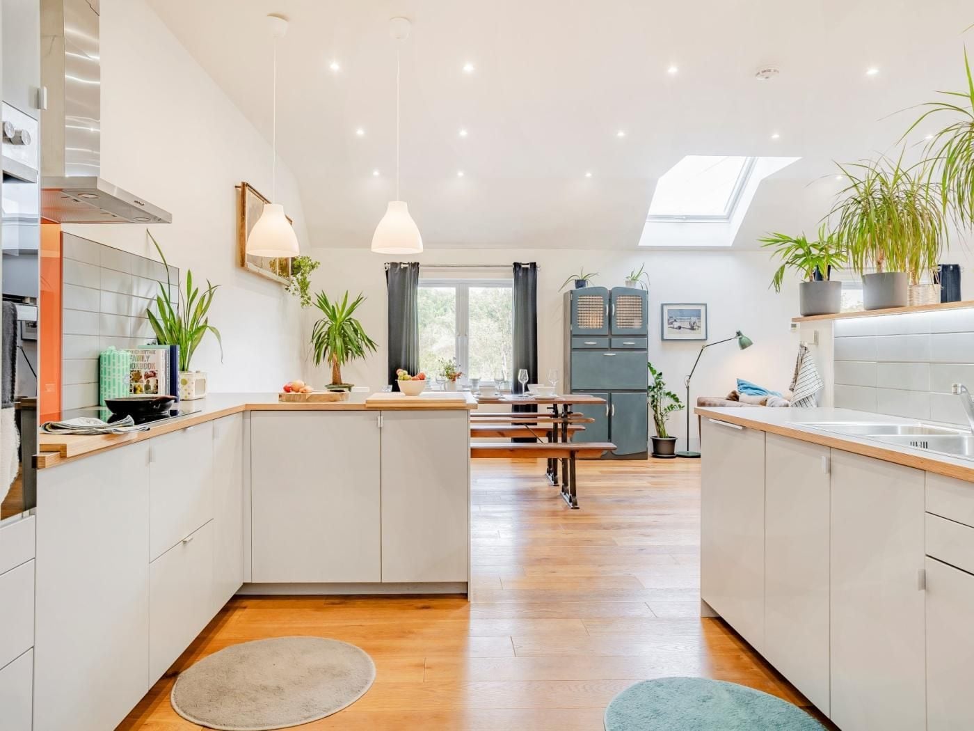 A modern kitchen with a central island, wooden flooring, and pendant lighting.
