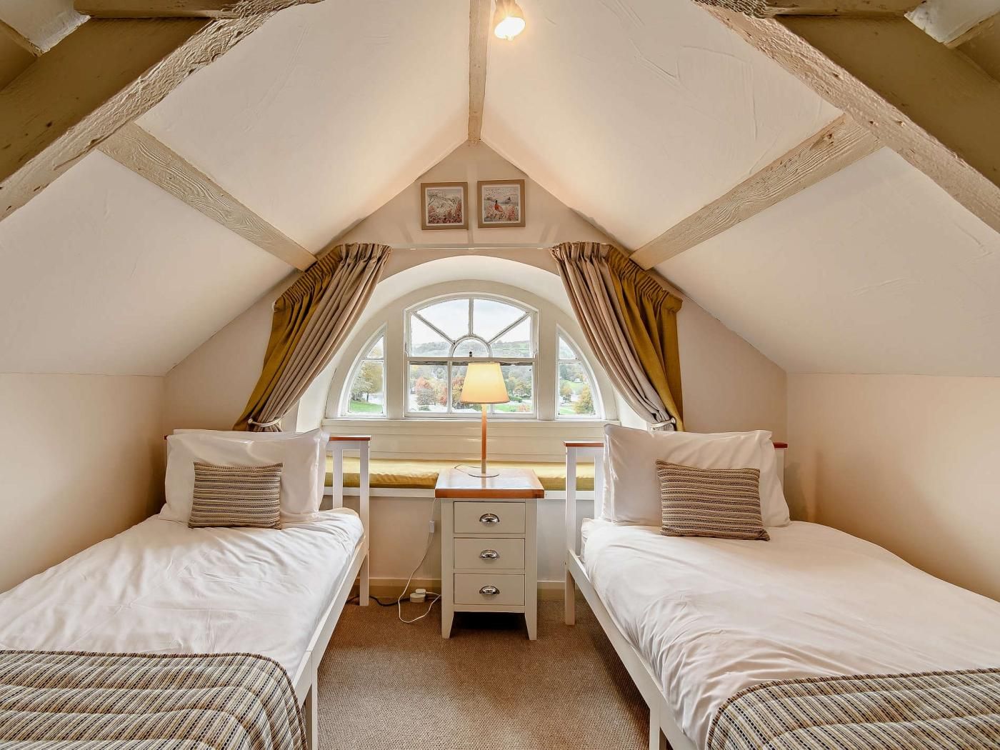 Une chambre avec deux lits simples, un bureau et une fenêtre avec des rideaux.