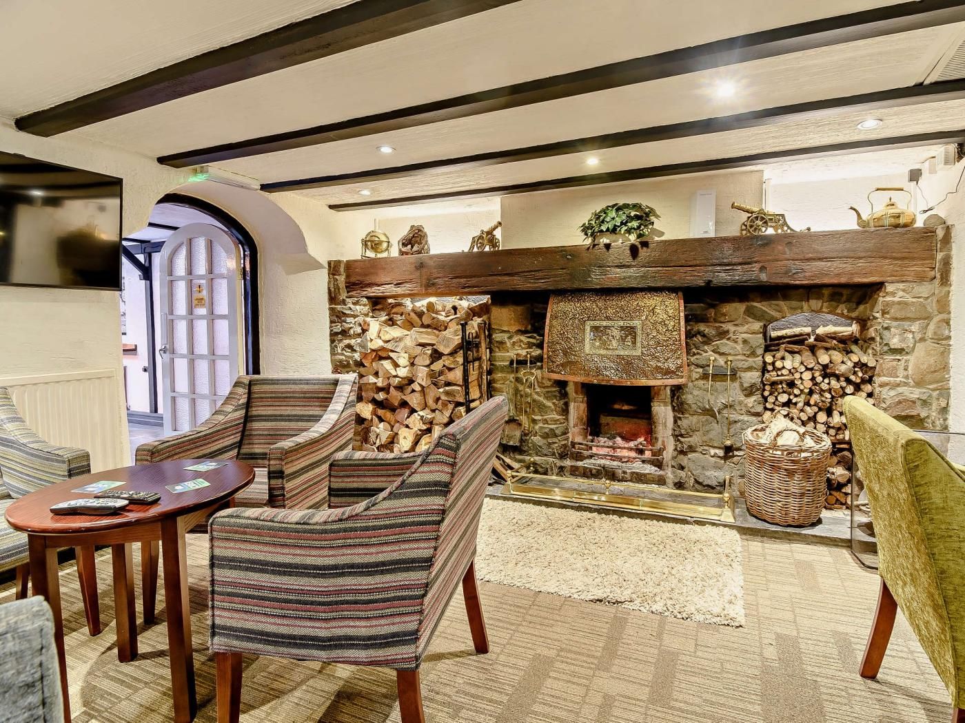 Una habitación acogedora con chimenea de piedra, sillones a rayas, una mesa de madera y vistas al exterior.