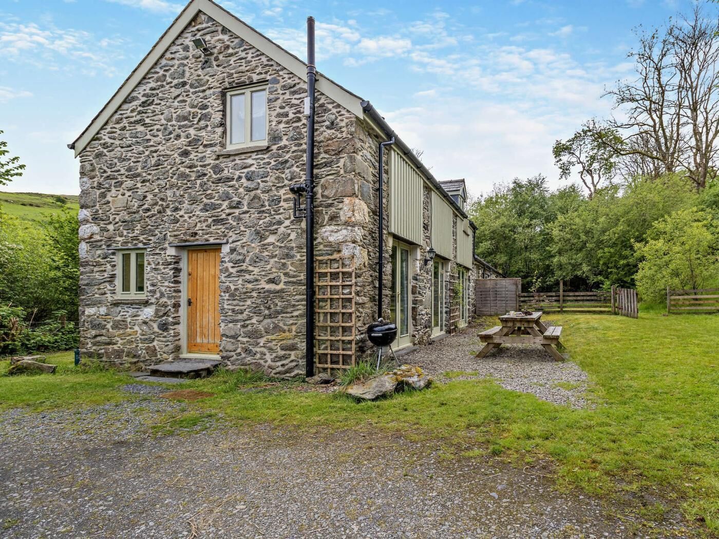 A stone building with a wooden door, a window, and a picnic table in the yard.