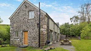 A stone building with a wooden door, a window, and a picnic table in the yard. - 2 Bed in Machynlleth (oc-93645) (Glaspwll)