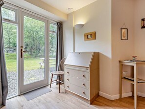 A room with a sliding glass door leading to an outdoor area, a wooden chair, a white dresser, a small table, and a wall-mounted light fixture. - 2 Bed in Machynlleth (oc-93645) (Glaspwll)