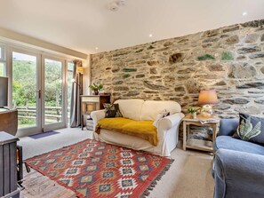 Ein gemütliches Wohnzimmer mit einer Steinwand, einer Couch, einem blauen Sessel, einem gemusterten Teppich und einem Kamin.