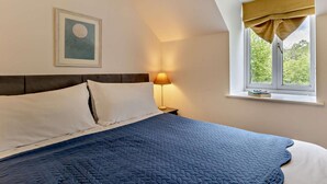 A bedroom with a bed, a nightstand, a lamp, a window with curtains, and a framed picture on the wall. - 2 Bed in Machynlleth (oc-93645) (Glaspwll)