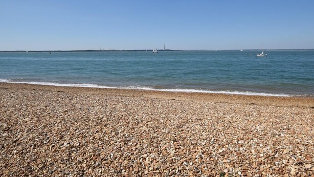 Ein Kiesstrand mit ruhiger See und entfernten Segelbooten.