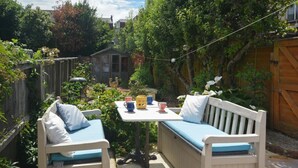 Eine Terrasse mit einer Holzbank und einem Tisch, umgeben von Grünpflanzen und einem Holzzaun.