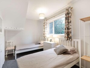 Ein Schlafzimmer mit zwei Betten, einem Sessel, einem Nachttisch, einer Lampe und einem Fenster mit Vorhängen.