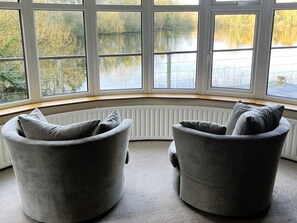 A corner room with two grey armchairs facing a bay window overlooking a lake. - 4 Bed in Peterborough (oc-93450) (Maxey)