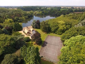 A residential property with a tennis court, surrounded by dense greenery and a river.