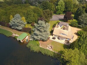 Una casa amb un gran jardí, una pista de tennis i una massa d'aigua.