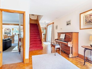 A spacious living area with a grand piano, a red carpeted staircase, and a dining area in the background. - 4 Bed in Peterborough (oc-93450) (Maxey)