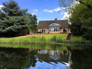 A house with a pond in front, surrounded by trees.
