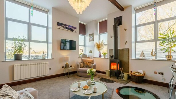 Een knusse woonkamer met een open haard, comfortabele zithoek, een televisie en grote ramen.