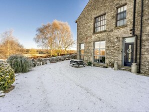 A stone building with a snow-covered patio, outdoor seating, and a view of trees and fields. - 1 Bed in Carnforth (oc-90528) (Yealand Redmayne)