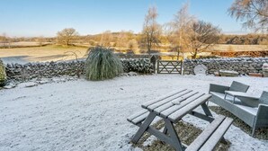 Een besneeuwde buitenruimte met een stenen muur, een houten poort en een picknicktafel.