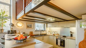 Een moderne keuken met een centraal eiland, een eethoek met stoelen, een trap en uitzicht op de omgeving.