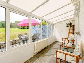 A conservatory with a view of a grassy field, a pink umbrella, and a wooden chair. - 3 Bed in Hawkshead (oc-llh40) (Hawkshead)