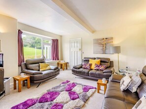 A living room with two leather sofas, a patterned rug, and a view of a green landscape through the window. - 3 Bed in Hawkshead (oc-llh40) (Hawkshead)