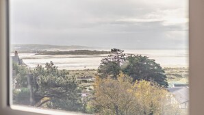A coastal view through a window, including a beach, trees, and distant hills. - 5 Bed in Aberdovey (oc-93603) (Aberdovey)