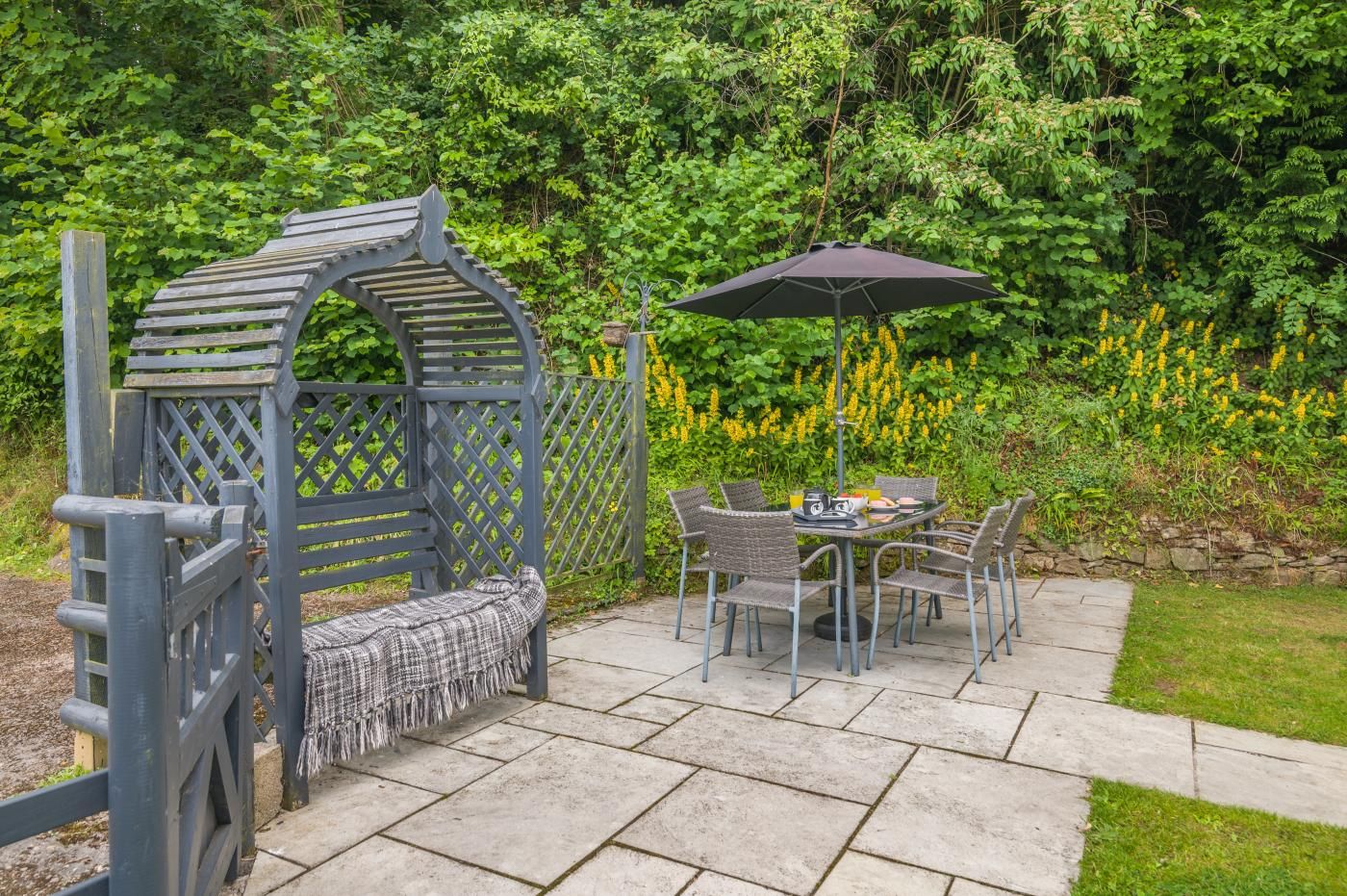 Une terrasse dotée d’une pergola en bois, d’une table avec des chaises et d’un parasol.