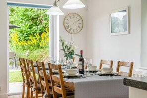 A dining area with a table set for four, a clock on the wall, and a window with a view of greenery. - 4 Bed in Ross -on- Wye (oc-72538) (Symonds Yat)