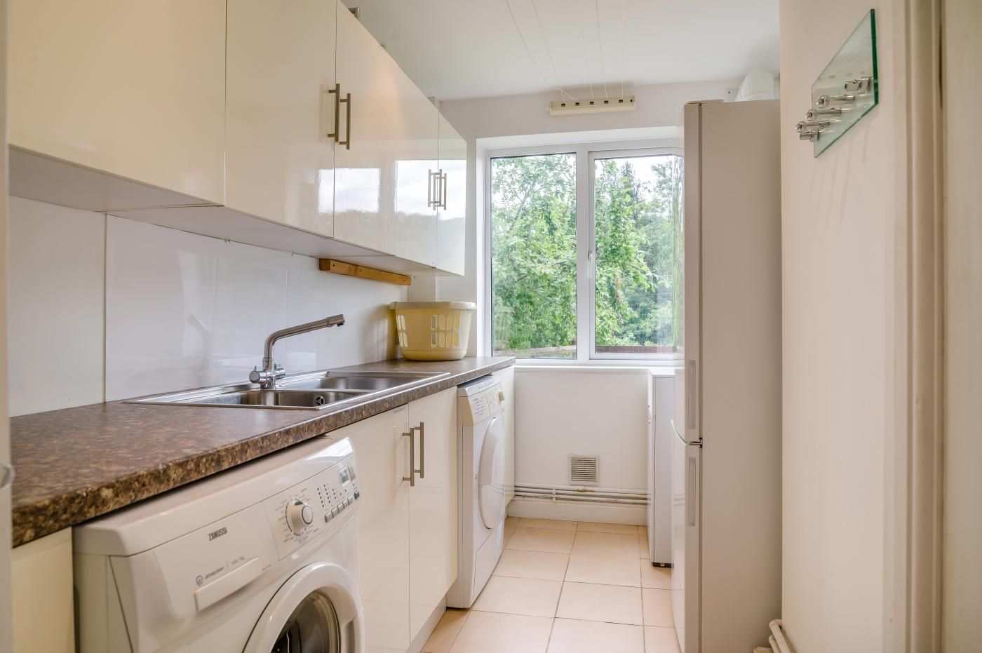 Une cuisine équipée d’un lave-linge, d’un évier et d’une fenêtre donnant sur un espace verdoyant.