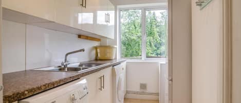 Una cocina con lavadora, un lavabo y un ventanal con vistas al verdor.