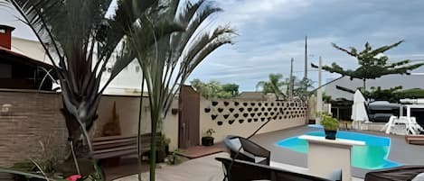 An outdoor patio with a pool, seating area, and potted plants.