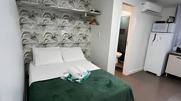 Una habitación pequeña y funcional con cama, kitchenette y baño.