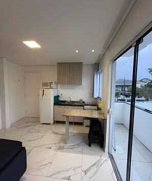 A modern kitchen with a dining area, a white refrigerator, and a view through a glass door. - Pousada da Mel (Florianópolis)