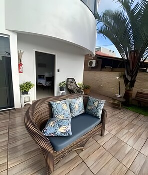 A modern outdoor seating area with a curved sofa and cushions, a fire extinguisher, and potted plants.