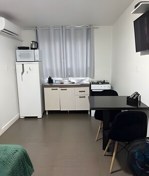 A compact kitchen with a microwave, kettle, and a small refrigerator. There is a dining table with chairs and a black fan on the floor. - Pousada da Mel (Florianópolis)