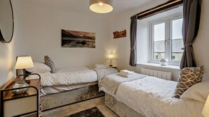 A bedroom with two beds, a window with curtains, a lamp, a painting, and a radiator. - 2 Bed in Carnforth (oc-90530) (Yealand Redmayne)