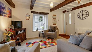 A living room with a sofa, a television, a clock, and a window with a view of the outside. - 2 Bed in Carnforth (oc-90530) (Yealand Redmayne)