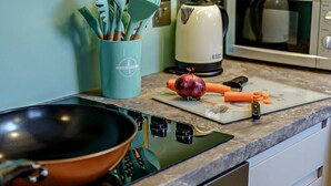 A kitchen with a stove, a digital clock, a cutting board with vegetables, and a kettle. - 2 Bed in Carnforth (oc-90530) (Yealand Redmayne)